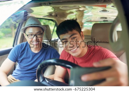 Handsome young friends taking picture of themselves on smartphone while sitting in car ready for unforgettable road trip