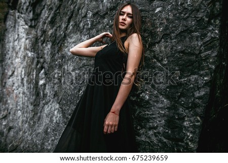 Girl in black dress on the background of the lake and rocks.