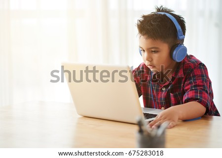 Cute little boy in headphones watching something on laptop at home