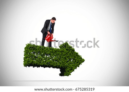 Businessman holding red watering can against arrow made of leaves