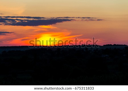 Orange sunset over silhouettes of village and trees