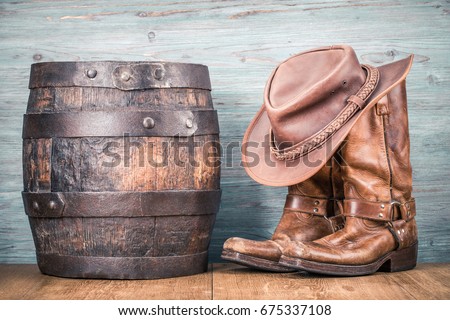 Wild West retro cowboy hat, old leather boots and aged oak barrel. Vintage style filtered photo