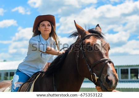 the young girl walks on the ranch. the slender girl in jeans and a cowboy's hat, nearby a horse. astride a horse