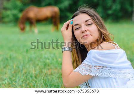 girl in white dress lying on stomach and looking into the distance. stay in the meadow . standing next to the horse and the guy . camping