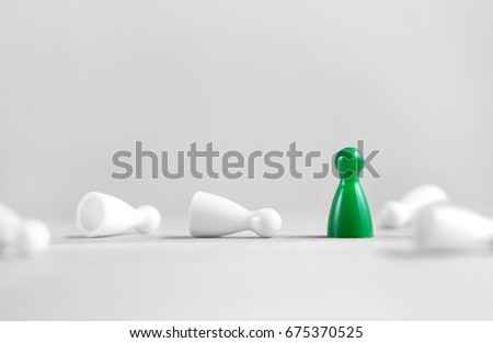Winning, victory, success and surviving concept. Green board game pawn stand alone, the white rest fallen. Eliminating competitors. One against the others. Last man standing. Against all odds. Royalty-Free Stock Photo #675370525