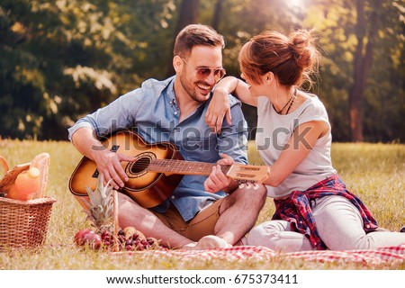 Picnic time. Young couple having fun with guitar on picnic in the park. Love and tenderness, dating, romance, lifestyle concept Royalty-Free Stock Photo #675373411