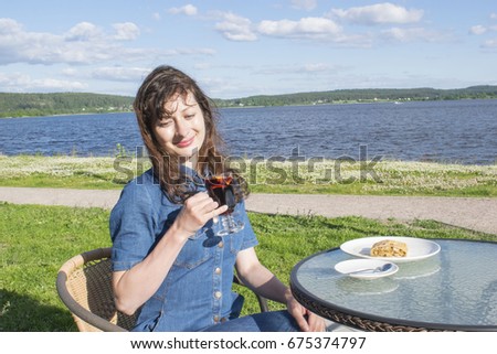 Beautiful young woman drinking mulled wine sitting in an outdoor cafe next to the lake. 