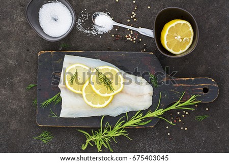 Raw cod before cooking on a black chopping Board with herbs and sea salt on a dark background. Top view.