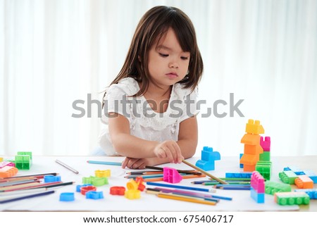 Waist-up portrait of cute Asian child wrapped up in drawing colorful picture with help of pencils, white background