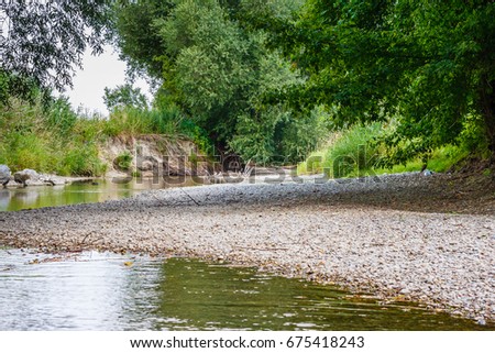 Picture is showing a little river with low water. The river is covered by trees on the left and on the right. Shows beautiful nature, shows calmness, atmospheric.