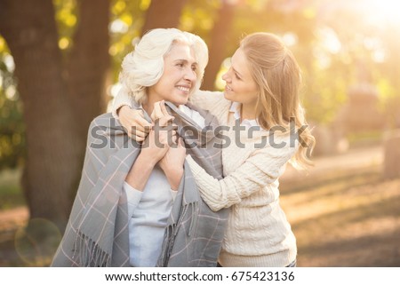 Loving young woman covering old mother with blanket outdoors Royalty-Free Stock Photo #675423136