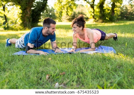 Closeup front view shot of an athletic couple working out together on a summer day. They are on exercise mat in city park in plank position while looking each other in the eyes. Time for plank