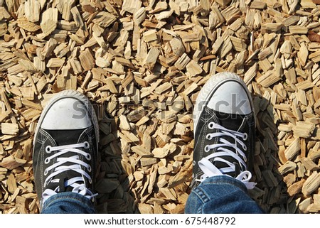 A top view of a man's legs and shoes standing on wooden chips.