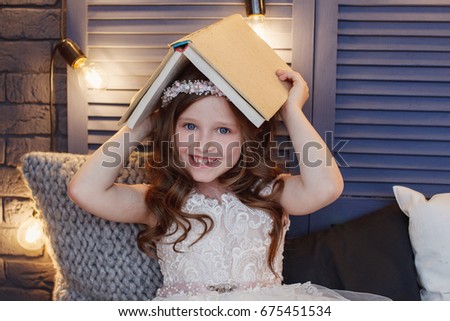Portrait of a beautiful little girl with curls and white Quinceanera dress reading a book