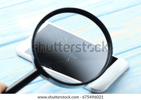 Broken smartphone in magnifying glass on a blue wooden table