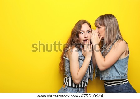 Two young woman whispering a secret on yellow background