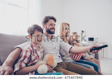 Leisure together. Happy family of four is enjoying at home. Small cute kids are with toys, parents are on the sofa, hugging, watching cartoons