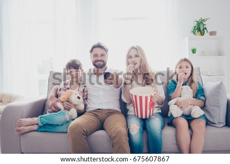 Fun time together. Happy family of four is watching interesting educational documentary, eating popcorn, at home on a couch