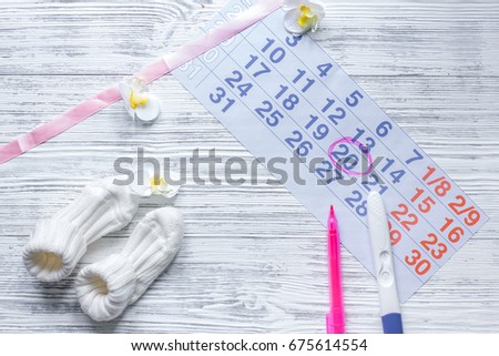 Pregnancy planning. Calendar, pregnancy test and booties on wooden background top view