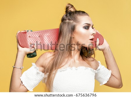 Trendy young woman having fun with longboard.Yellow background.