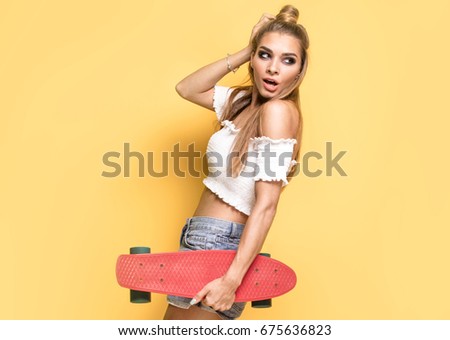 Trendy young woman having fun with longboard.Yellow background.