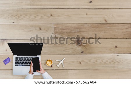Top view man's hands using smartphone and laptop with coffee cup, Airplane, Photos and Credit card on wooden table at office. Shopping online and business concept.