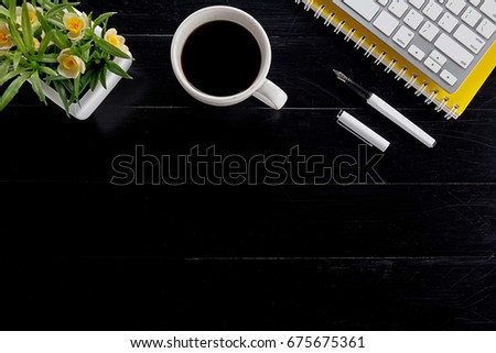 Office desk table with pen, keyboard on notebook, cup of coffee and flower. Top view with copy space (selective focus).