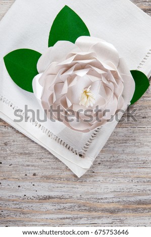 PAPER FLORAL ART. Decorative hand made paper white camellia flower on napkin over wooden table background