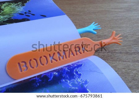 Colorful plastic bookmark used to mark reading location after stop reading the book. It was design with image of colorfull hand and has word 'bookmark' on it.  

