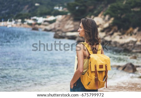 Back view hipster girl with backpack in sand coastline on nature landscape, mock up. Traveler on background beach seascape and horizon mountain. Tourist look on blue sun ocean, summer relax lifestyle 