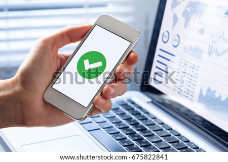 Hand holding a smartphone with a green checkmark icon on the screen to show a validated, confirmed, completed or approved status Royalty-Free Stock Photo #675822841
