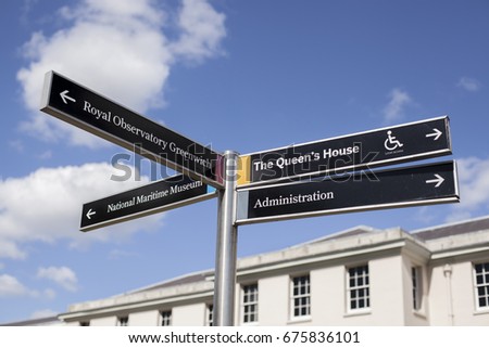 London signpost with destinations in Greenwich park with sunny sky and maritime museum on background