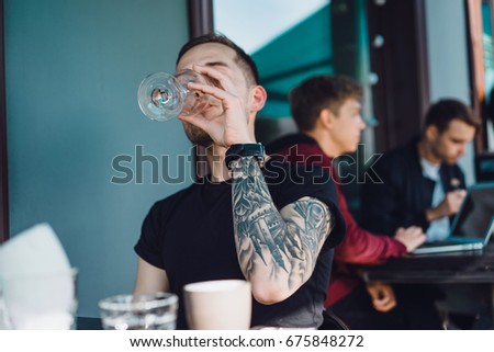 Handsome tattooed man on a summer terrace in a city cafe is drinking wine. Street Cafe.
