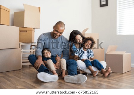 Happy family with two children having fun at new home. Young multiethnic parents with two sons in their new house with cardboard boxes. Smiling little boys sitting on floor with mother and dad. Royalty-Free Stock Photo #675852163