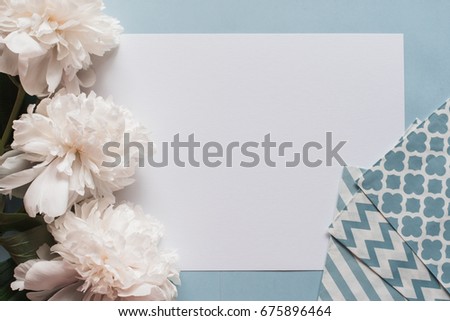 Gogreous white peonies flowers and empty tag on blue background. Flat lay. Top view with copy space and a brush for watecolor text. Selective focus.