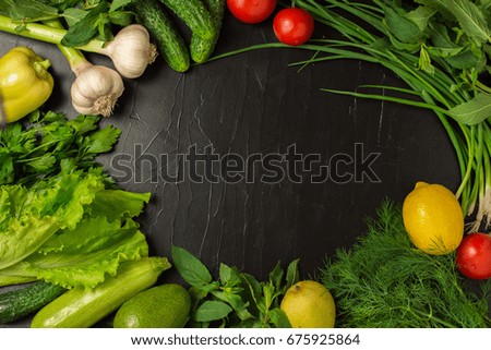 Frame of fresh vegetables, fruits and greens on black background. Top view. Vegetarian food - tomato, lemon, onion, dill, parsley, garlic, mint, salad, cucumber, avocado, zucchini.