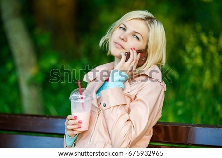 Girl with milkshake talking on phone sitting on bench at street in summer