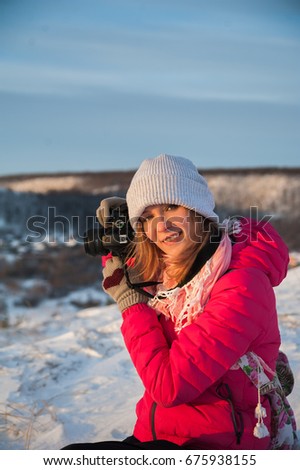 Girl tourist in a red jacket photographs the winter landscape on the camera. The tourist takes a picture of the dawn in the morning. A girl in a gray hat takes a picture of the morning city Saratov