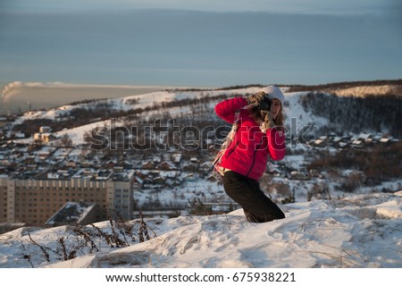 Girl tourist in a red jacket photographs the winter landscape on the camera. The tourist takes a picture of the dawn in the morning. A girl in a gray hat takes a picture of the morning city Saratov