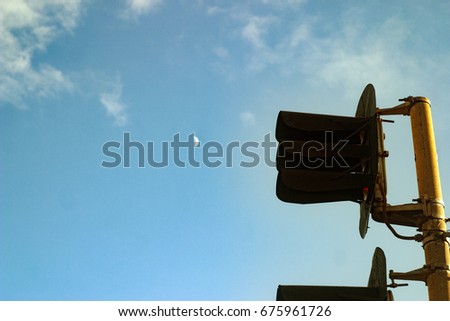 Black old semaphore signal at the railway station, against a background of a summer blue sky with white clouds and the moon.
