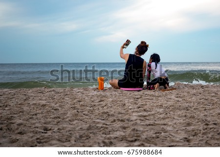 Mother and daughter enjoying vacation taking picture on cell phone by the beach in Thailand