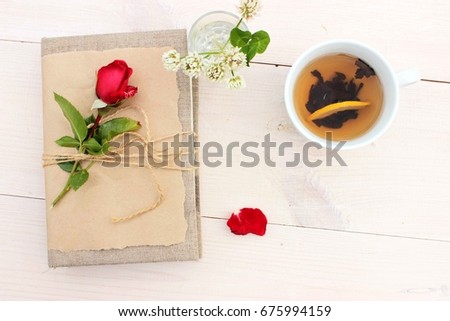 Notebook to write some memories, dreams, secrets or wishes decorated with beautiful red rose and cup of hot tasty tea with lemon. Romantic decor, lifestyle concept. Craft theme