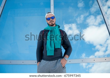 Outside Portrait of an Handsome Young Man in Sunglasses on Skyscraper Background. The window Reflects the Blue Sky. Boy Looks at the Camera.