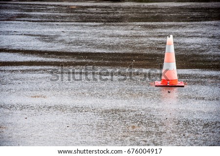 A road cone with broken top placed on asphalt on the right side of the photo. Cone reflects in the wet asphalt surface
