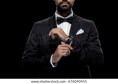 cropped view of businessman in bow tie and tuxedo with watch, isolated on black  Royalty-Free Stock Photo #676040455