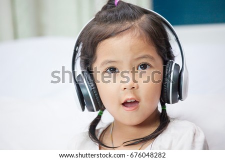 Cute asian child girl in headphones listening the music and sing a song in her room