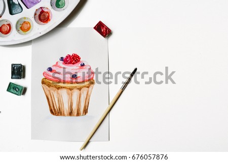Designer workplace. Watercolor cupcake painted card with various drawing equipments. Flat lay, top view. Artist workspace