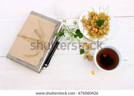 Notebook to write some memories, dreams, secrets or wishes, small bunch of wild white clover and plate with fresh yellow currants berry and cup of tea. Romantic decor, lifestyle theme
