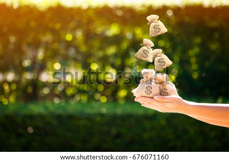 Women hands hold a money bags and dropping on the top in the public park for loans to planned investment in the future concept. Royalty-Free Stock Photo #676071160