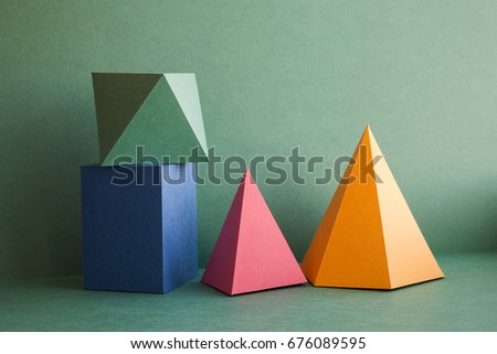 Abstract geometrical solid figures still life. Colorful three-dimensional pyramid prism rectangular cube arranged on green background. Yellow blue pink malachite colored objects textured paper surface